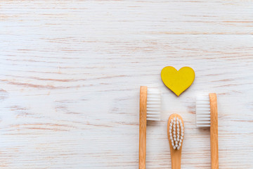 Three wooden bamboo toothbrushes for family and wooden hearts on white wood background, copy space