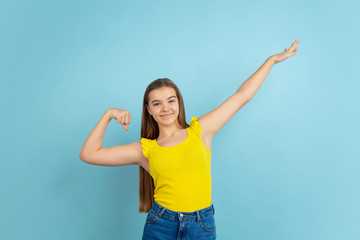Successful winner. Caucasian teen girl's portrait isolated on blue background. Beautiful model in casual yellow wear. Concept of human emotions, facial expression, sales, ad. Copyspace. Looks cute.