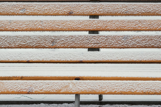 The park bench is covered with a thin layer of fluffy snow.