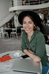 Hipster woman in lovely cafe drinking coffee and looking at camera. Vertical image. Freelancer,...
