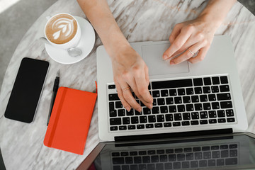 Hands of business woman on laptop computer keyboard. Coffee, mobile phone and notebook. Freelancer,...
