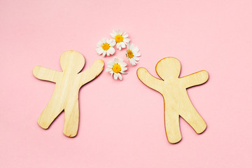 children wooden toy people and fresh summer chamomile flowers on pastel pink background, love, friendship, dating symbol, top view, flat layout