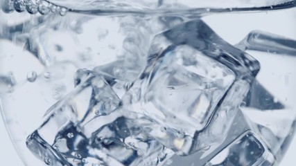 Ice cubes with bubbles under water in glass, close up slow motion