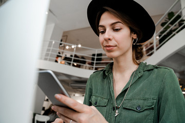 Successful concentrated woman searching mobile phone, looking trendy and fashionable. Freelancer, entrepreneur, work in cowering space, public place, modern people lifestyle, business online concept.