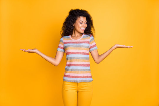 Portrait of her she nice attractive cheerful cheery wavy-haired girl in striped tshirt holding on palms two invisible objects weighing isolated on bright vivid shine vibrant yellow color background