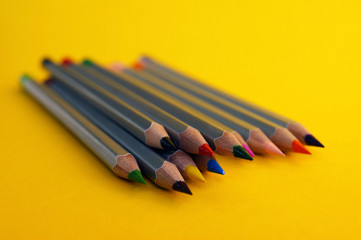 Many colorful pencils laying on yellow background.