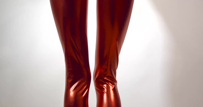 Upcoming tracking shot of the hips of very slender and thin unrecognizable girl in a tight fitting shiny red zentai suit, shaking her hips. Isolated on  white studio background. 4k 50 fps slow motion