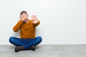 young handsome man covering face with hand and putting other hand up front to stop camera, refusing...