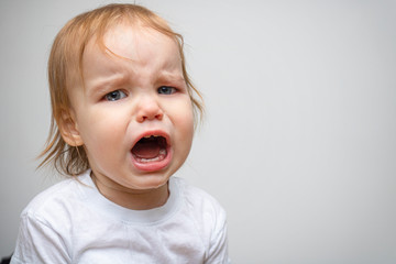 Portrait of a baby toddler child crying. Kid opened his mouth wide, in which fangs erupt and saliva flows. The child has toothaches and a crisis of 1 year of life. Copy space text, banner, close-up