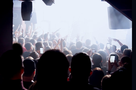 Audience With Hands Raised At A Music Festival With Colored Lights Streaming Down From Above The Stage. Rock Or Rap Concert With Many People.