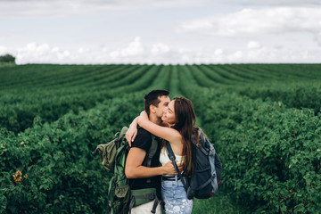 Portrait of happy young couple with backpacks on the field in spring. Man and woman walking in currant plantations