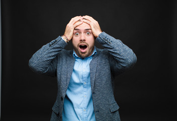 young businessman feeling horrified and shocked, raising hands to head and panicking at a mistake...