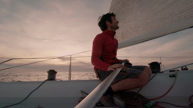 Happy authentic sailor or yachtsman steer sail boat on cinematic epic sunset in open sea. Life in ocean, search for adventure. Sailing vacation or sail school. Freedom and outdoor lifestyle