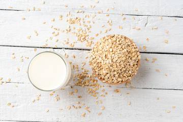 Glass of oat milk on white wooden background with rolled oatmeals. Top view. Close up