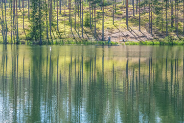 sky and tree reflection in secluded area by the lake. Calm waters and cloudy sky. fisherman in the background Sweden. selective focus. long exposure