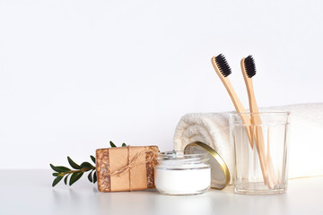 Bamboo toothbrushes in glass, natural tooth powder, soap and towel on light gray table. Zero waste bathroom accessories, eco friendly morning routine and sustainable lifestyle concept. Copy space.