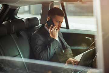 young businessman works in his laptop conducting phone conversation with assistant while sitting in...