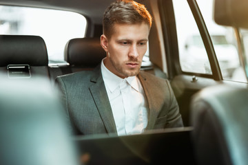 young businessman works in his laptop while sitting in his car on his way to office, multitasking concept