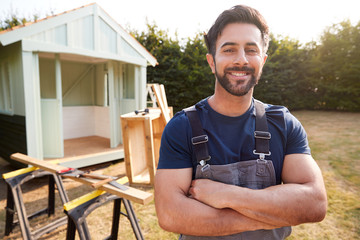 Portrait Of Male Carpenter Building Outdoor Summerhouse In Garden