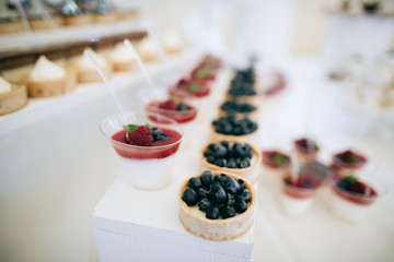 Candy bar at a party or wedding ceremony with delicious sweet cakes with strawberries and cream