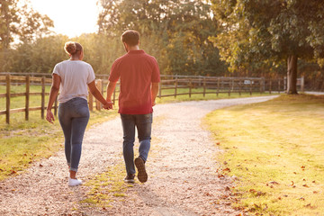 Fototapeta premium Rear View Of Romantic Couple Walking Hand In Hand Along Country Lane At Sunset