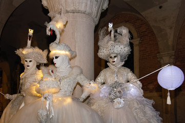 Three  masked persons at the carnival in Venice by night.