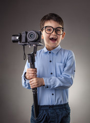 Cute kid with electronic steadicam shoots video on the gray background