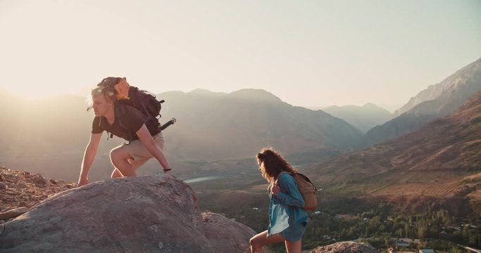 Young caucasian couple backpacking together, helping each other on way up, exploring beautiful mountains - adventure, freedom concept 4k footage