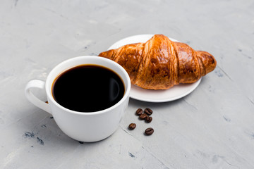 Coffee cup and croissant on gray stone background. Perfect breakfast in the morning. Rustic style, top view, food banner, selective focus