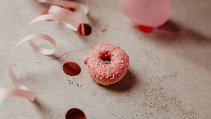 Donut in zartem rosa und bunten Streuseln mit Konfetti, Geschenkband und Luftballons auf hellem...