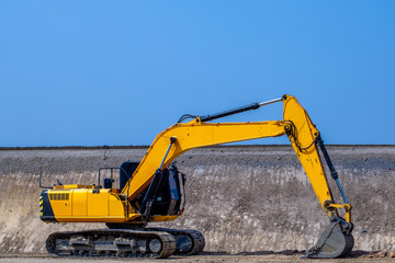 The big yellow backhoe is working on the ground at the outdoor construction project with the blue sky background in the sunny day. 