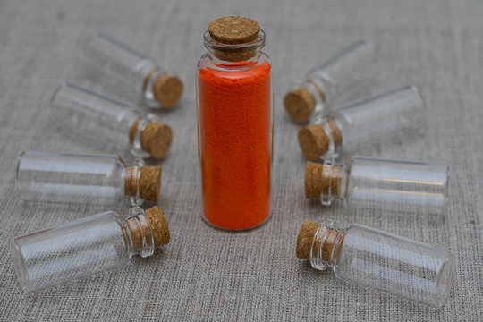 Red powder and crystalls crystals in small bottle on gray linen background
