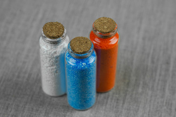 Blue, red and white powder and crystalls crystals in small bottles on gray linen background