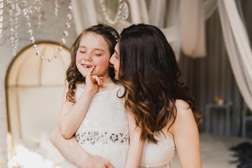 Mother and daughter hugging and playing together. Pretty little girl and beautiful woman. Girls in lace dresses playing in decorated room. Family weekend, beauty day, having fun, love concept.