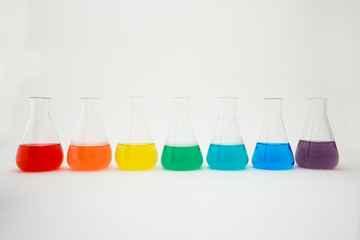Scientific laboratory glass erlenmeyer flask filled with colorful liquid forming rainbow on white...