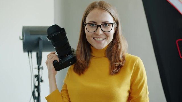 Portrait of successful female photographer beautiful young woman holding camera standing alone in studio. People, occupation and workplace concept.