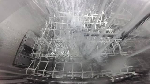 Slow motion. The master repairs the dishwasher and checks the operation of the nozzle mechanism, which rotates and sprays water. The process inside the dishwasher. Inside view of a dishwasher.