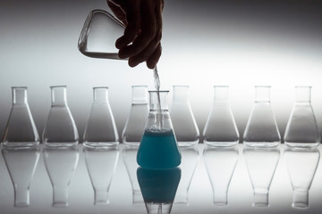 Hand pouring white in to blue liquid in scientific laboratory glass erlenmeyer flask with glassware...