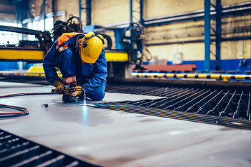 Worker cutting metal, steel with acetylene torch in big factory.