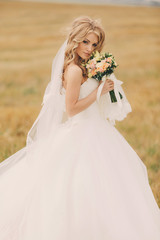 Fototapeta na wymiar beautiful young bride in luxury white wedding dress with roses bouquet. Portrait of a cute bride in summer field. happy Wedding day. Beautiful bride with makeup and hairstyle.