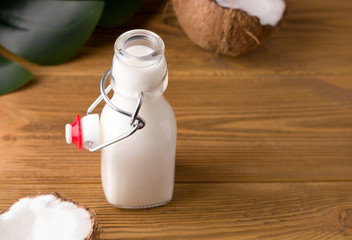 coconut milk on a wooden background in a glass bottle on a wooden background next to coconut halves