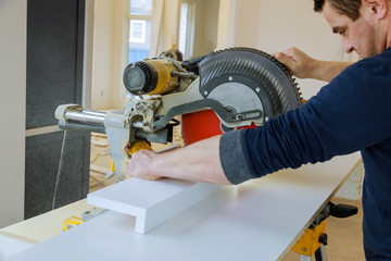 Worker cuts wood baseboard on the power saw