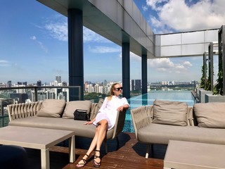 Woman in white dress with sunglasses sitting in lounge on rooftop before pool, Singapore, South East Asia