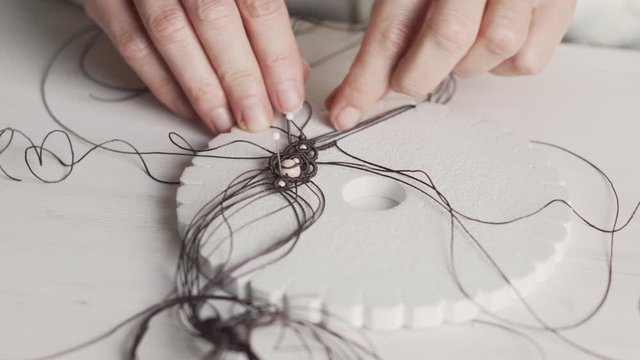 Lifestyle concept, work from home to reinvent your life: close-up of woman hands making macrame knotted jewelry with stone beads and tools on light wooden table