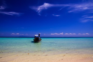 Fototapeta na wymiar Panoramic view from sand beach over shallow turquoise water and isolated thai long-tail boat into endless horizon with blue sky - Ko Phi Phi, Thailand