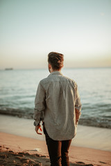 Joven de espaldas en la playa con la puesta de sol