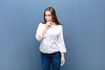 young blonde pretty girl asking for silence and quiet, gesturing with finger in front of mouth,...