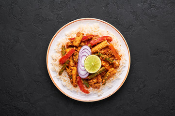 Vegetable Jalfrezi with basmati rice in white plate at black slate background. Jalfrezi is Indian Cuisine dish with stir fried vegetables and tomato-nuts gravy with spices. Indian Food. Top view