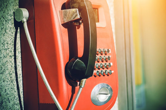 Street retro red vending machine with phone, illuminated by bright sunlight.