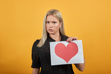 Beautiful blonde girl in black dress on yellow background upset woman dissatisfied holding piece of...